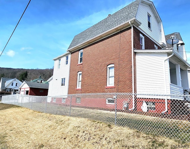 view of home's exterior featuring a lawn, a gambrel roof, roof with shingles, fence, and brick siding