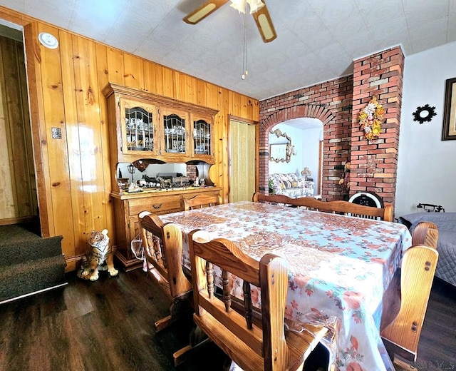 dining room with wood walls, ceiling fan, baseboards, and dark wood finished floors