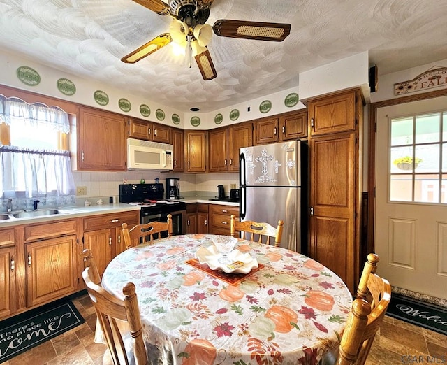 kitchen with white microwave, electric range, a sink, freestanding refrigerator, and brown cabinets