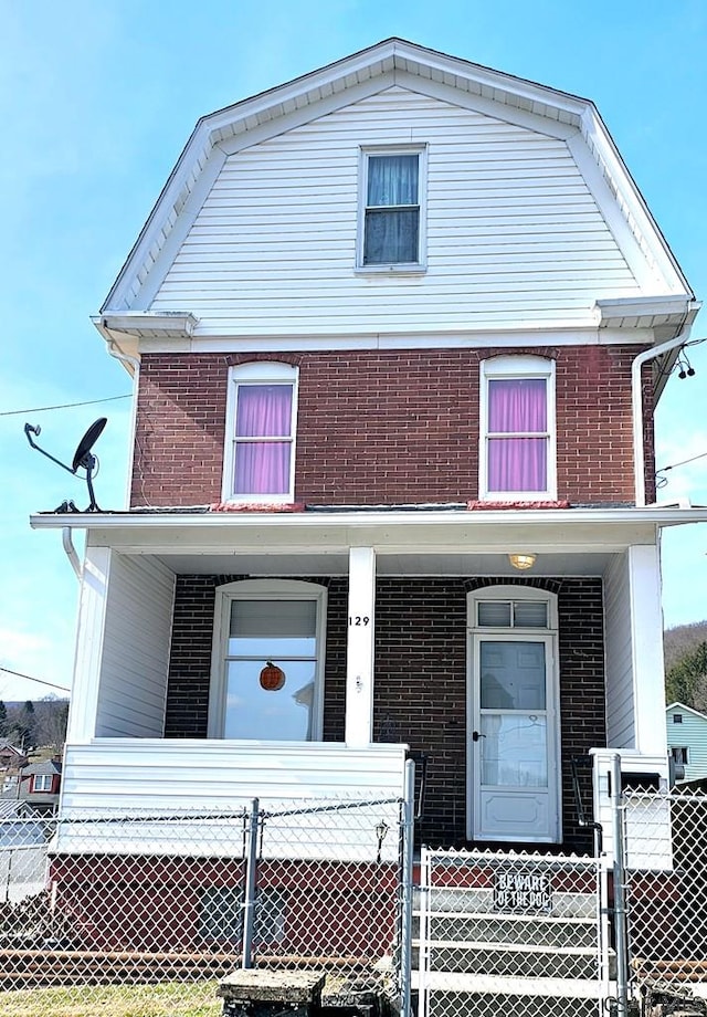 view of front facade featuring brick siding, a porch, and a gambrel roof