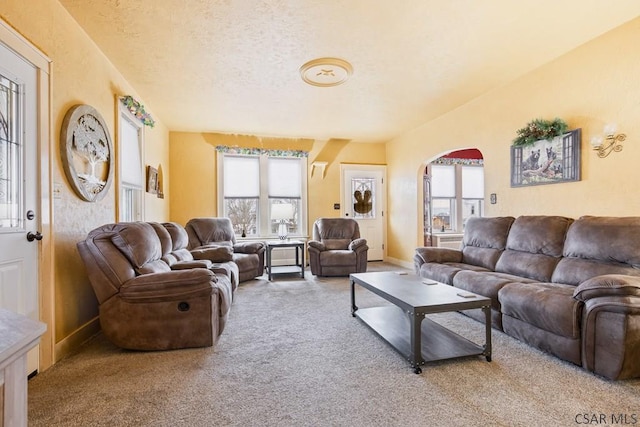 carpeted living room with arched walkways, a textured ceiling, and baseboards