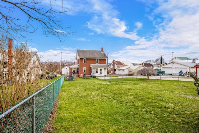 rear view of house featuring a fenced backyard, a residential view, a detached garage, a yard, and a chimney