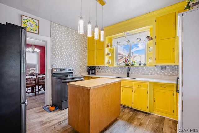 kitchen featuring a notable chandelier, a sink, freestanding refrigerator, range with electric cooktop, and wallpapered walls