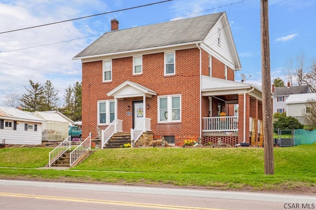 view of front facade with a front lawn, a chimney, covered porch, and brick siding