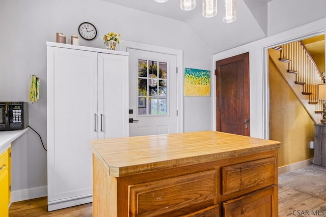 kitchen featuring black microwave, baseboards, light wood finished floors, and vaulted ceiling