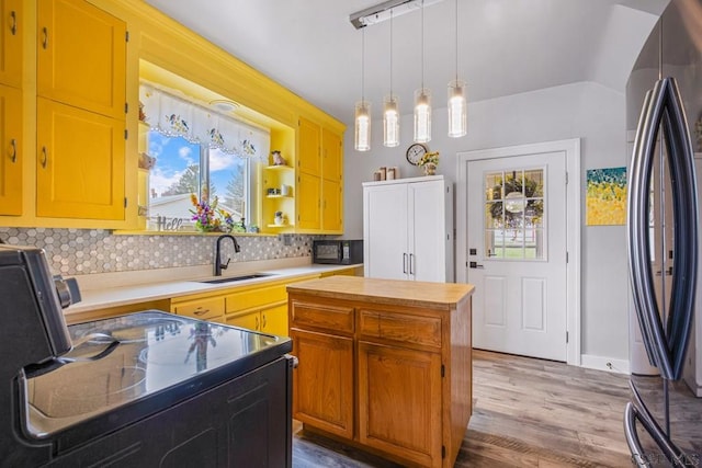 kitchen with backsplash, a sink, hanging light fixtures, light wood-style flooring, and black appliances