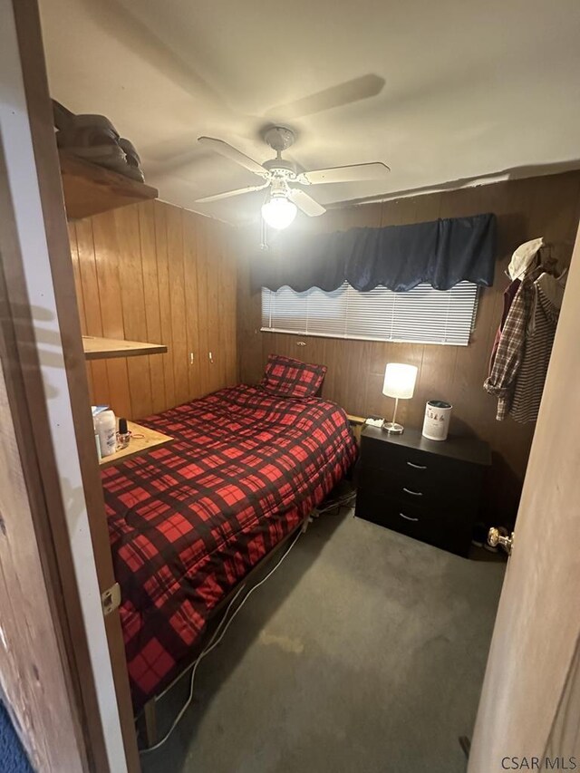 carpeted bedroom featuring wooden walls and ceiling fan