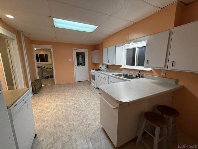 kitchen with sink, white cabinetry, a paneled ceiling, kitchen peninsula, and white appliances