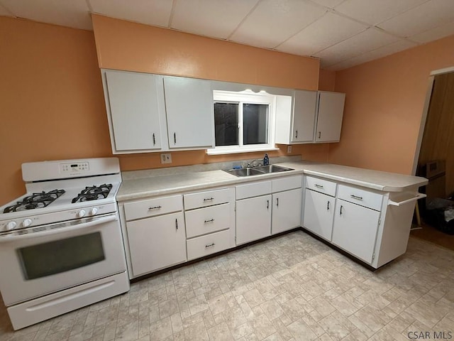 kitchen featuring sink, white cabinets, a drop ceiling, white gas range, and kitchen peninsula