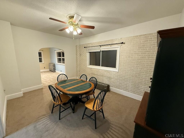 carpeted dining space featuring brick wall, radiator heating unit, a textured ceiling, and ceiling fan