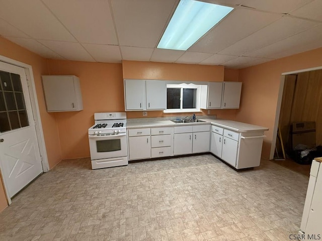 kitchen featuring white gas range, a paneled ceiling, sink, and white cabinets