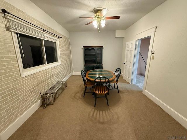 dining area featuring radiator, carpet, ceiling fan, and brick wall