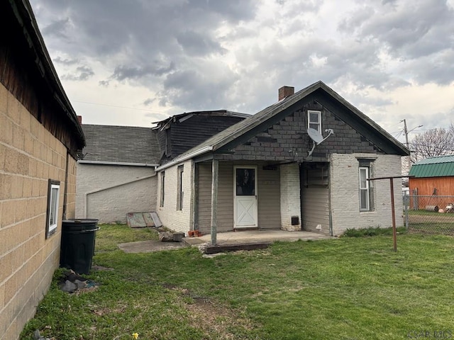 back of house featuring a yard, a patio, fence, a chimney, and a shingled roof
