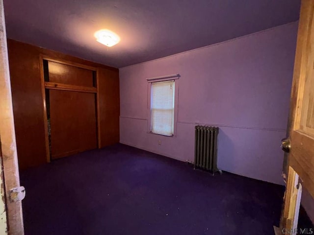 unfurnished bedroom with radiator heating unit and a closet