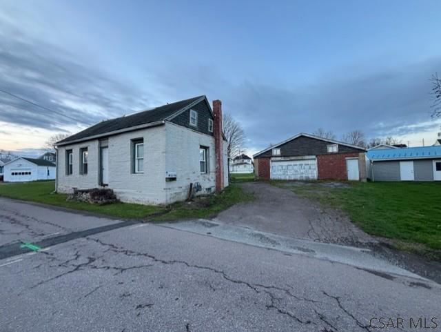 view of front of house featuring an outdoor structure, a chimney, driveway, a front yard, and a garage