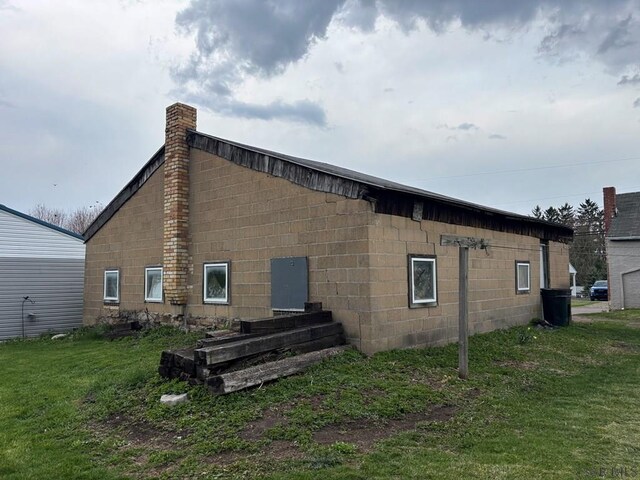 rear view of house featuring concrete block siding, a chimney, and a lawn