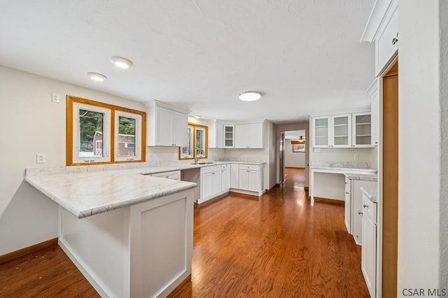 kitchen featuring dark wood finished floors, glass insert cabinets, white cabinets, a sink, and a peninsula