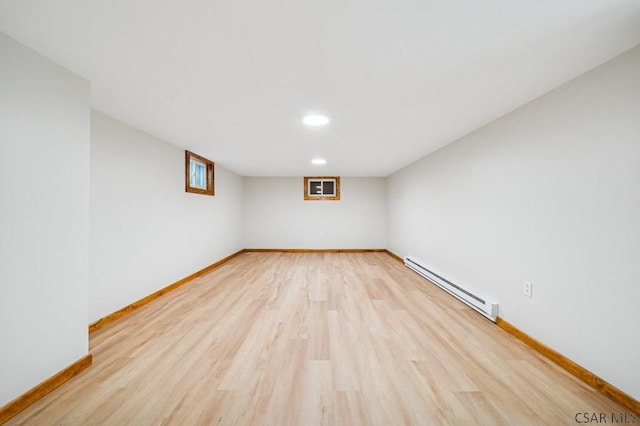 basement with a baseboard radiator, baseboards, and light wood finished floors