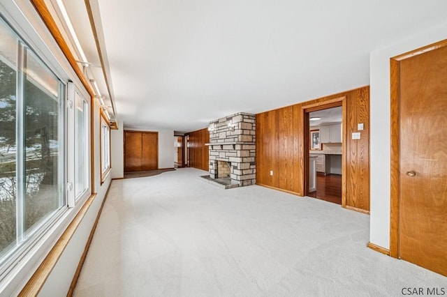 unfurnished living room with carpet, wooden walls, and a stone fireplace