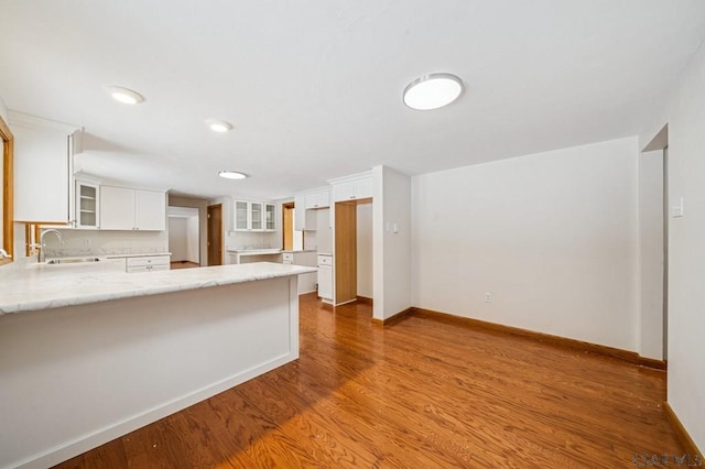 kitchen with a peninsula, wood finished floors, glass insert cabinets, and white cabinetry