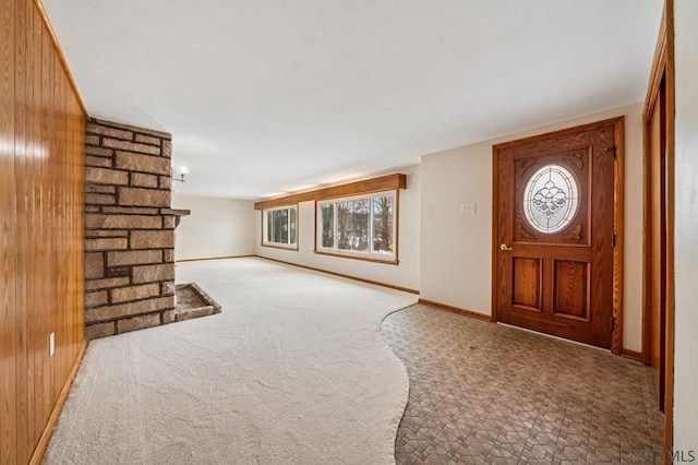 foyer entrance featuring wood walls, carpet, a fireplace, and baseboards