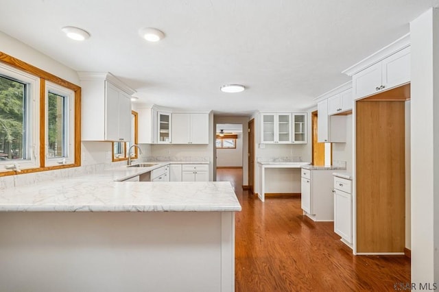 kitchen featuring dark wood-style flooring, glass insert cabinets, white cabinetry, a sink, and a peninsula