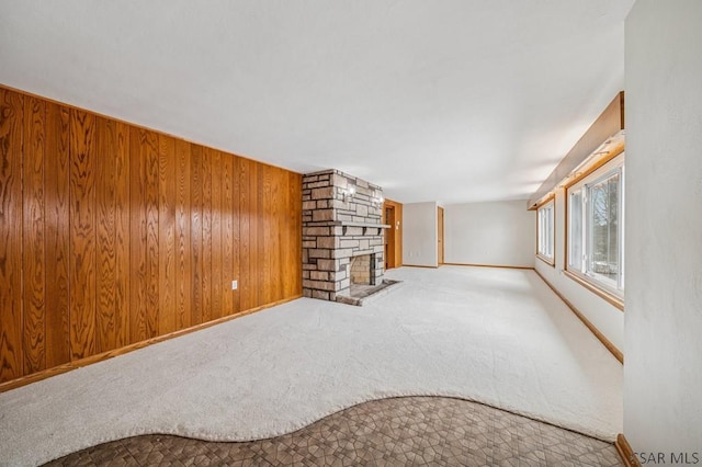 unfurnished living room featuring carpet flooring, wood walls, a stone fireplace, and baseboards