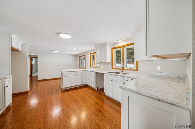 kitchen with light wood-type flooring, white cabinetry, a sink, and a peninsula