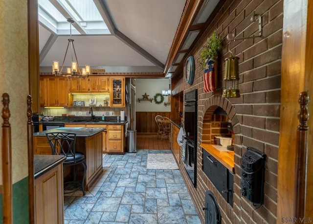 kitchen featuring pendant lighting, vaulted ceiling with skylight, sink, a chandelier, and a kitchen breakfast bar