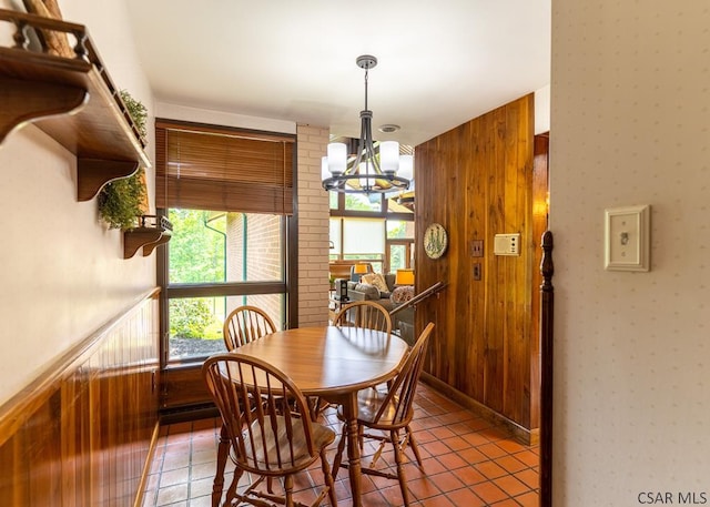 tiled dining room featuring a chandelier and wood walls