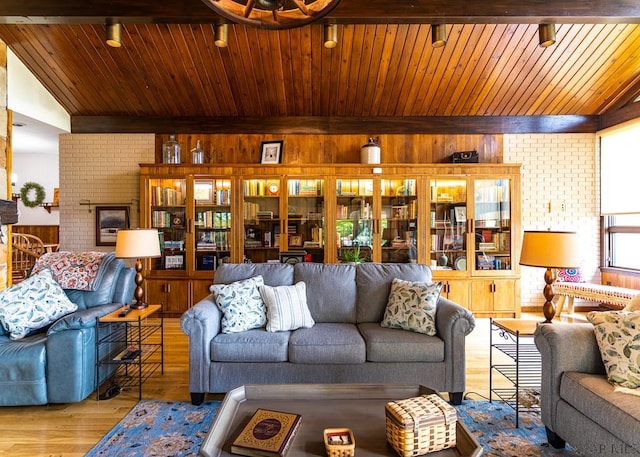 living room featuring lofted ceiling with beams, brick wall, a fireplace, and light hardwood / wood-style floors