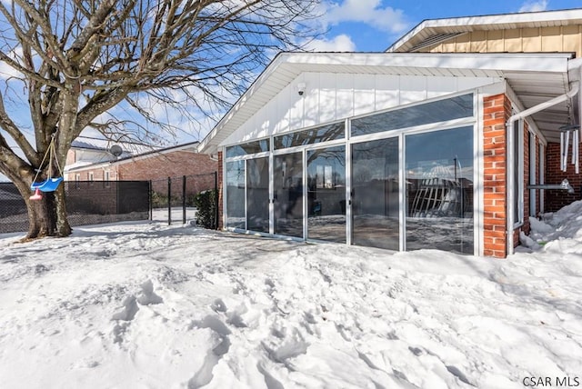 snow covered back of property with a sunroom