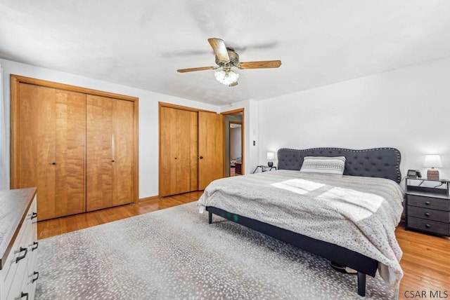 bedroom with ceiling fan, light hardwood / wood-style flooring, and two closets