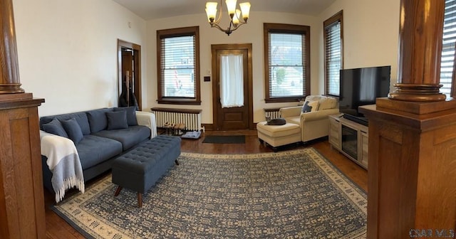 living room with dark wood-type flooring, radiator, decorative columns, and a notable chandelier