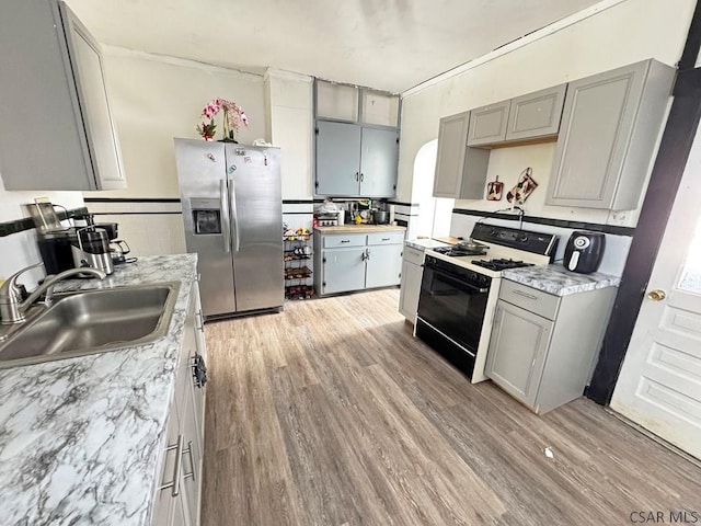 kitchen with sink, gas range, gray cabinetry, and stainless steel refrigerator with ice dispenser