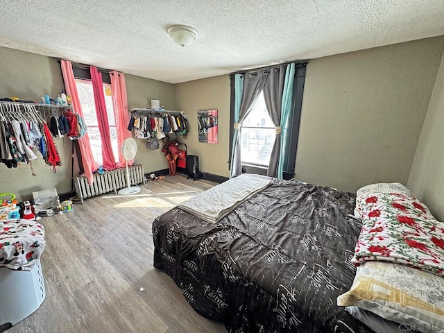 bedroom with radiator heating unit, multiple windows, a textured ceiling, and hardwood / wood-style floors