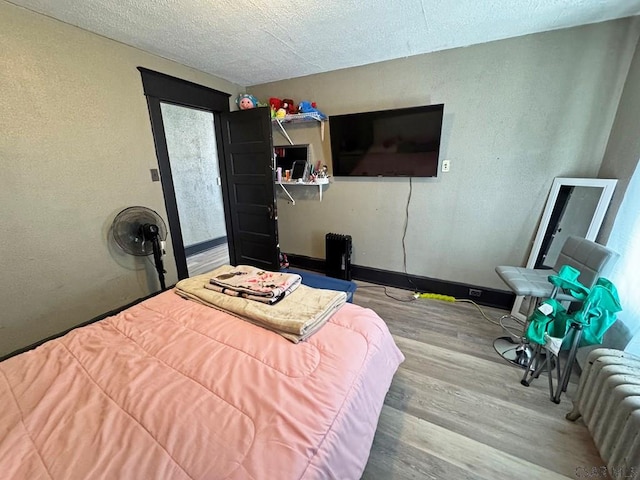 bedroom featuring a textured ceiling, hardwood / wood-style flooring, and radiator heating unit