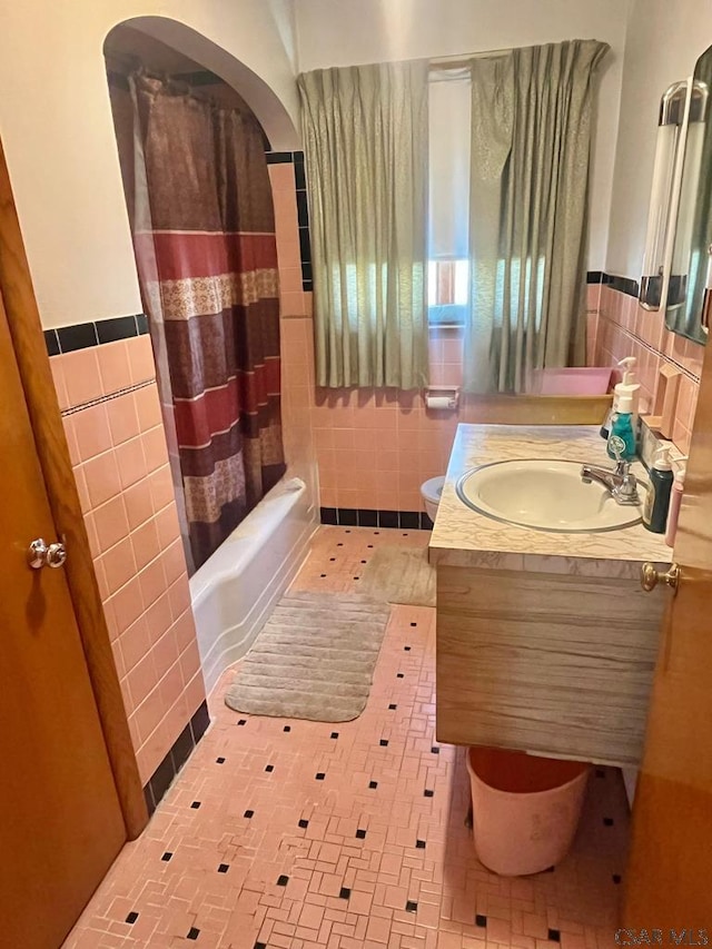 bathroom with toilet, tile walls, wainscoting, shower / tub combo, and vanity