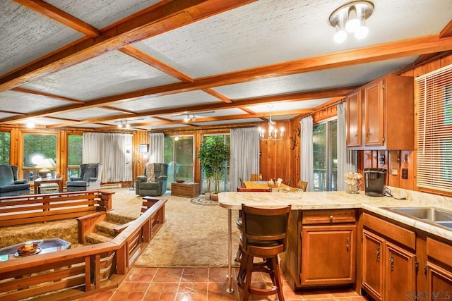 kitchen with coffered ceiling, wood walls, a chandelier, kitchen peninsula, and pendant lighting