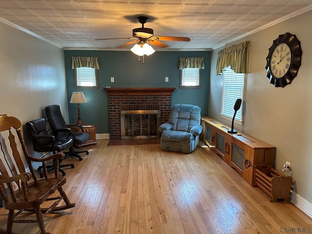 living area with crown molding, ceiling fan, a fireplace, and light wood-type flooring