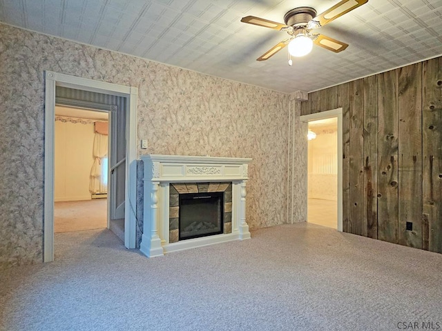 unfurnished living room with a tile fireplace, wood walls, ceiling fan, and carpet