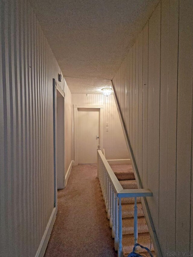 corridor featuring a textured ceiling, carpet, and wood walls