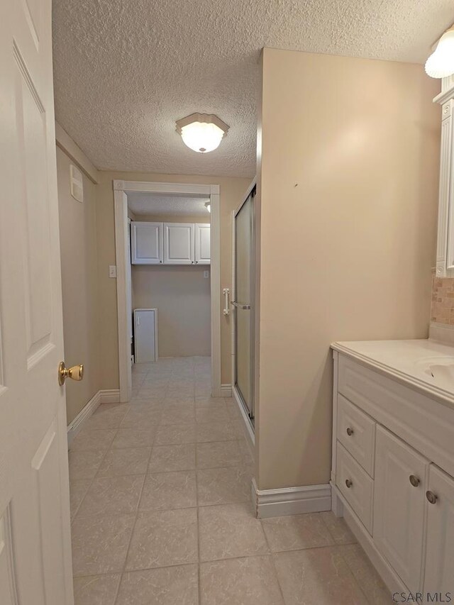 bathroom with a shower with door, vanity, and a textured ceiling