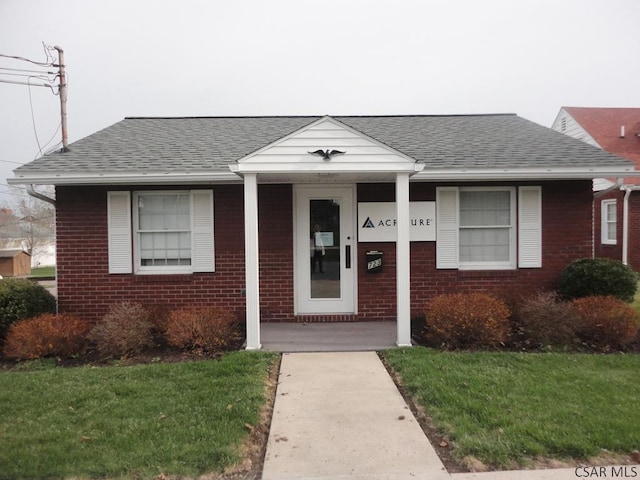 bungalow with a front yard, a shingled roof, a porch, and brick siding