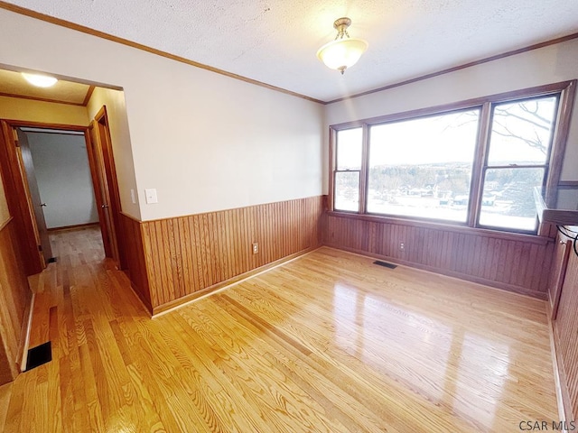 spare room with ornamental molding, wooden walls, light hardwood / wood-style floors, and a textured ceiling