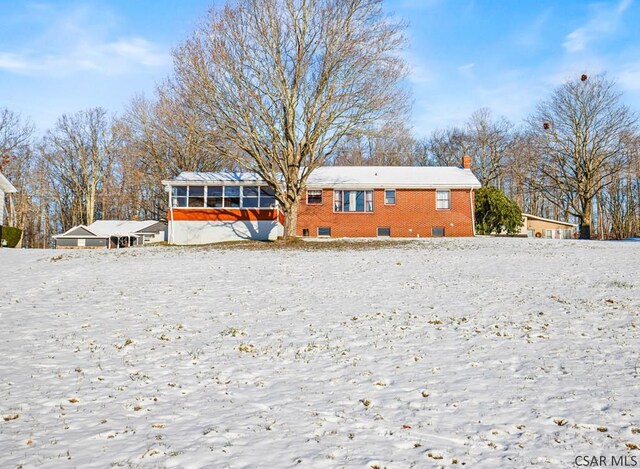 snow covered back of property with a sunroom