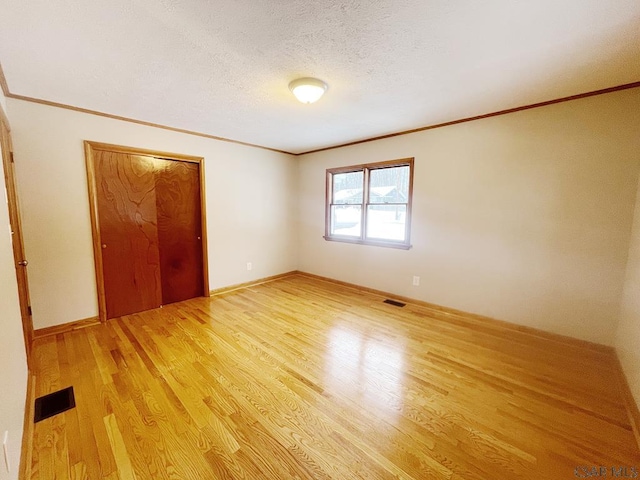 unfurnished bedroom featuring crown molding, light hardwood / wood-style flooring, a closet, and a textured ceiling