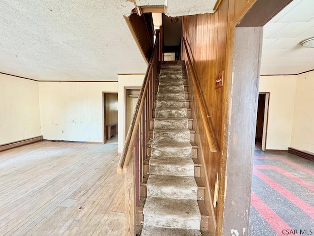 staircase featuring wood-type flooring, wooden walls, and a textured ceiling