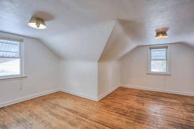 additional living space featuring lofted ceiling, a textured ceiling, and light hardwood / wood-style flooring