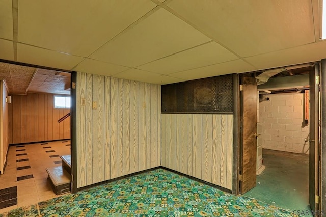 basement featuring a paneled ceiling and wood walls